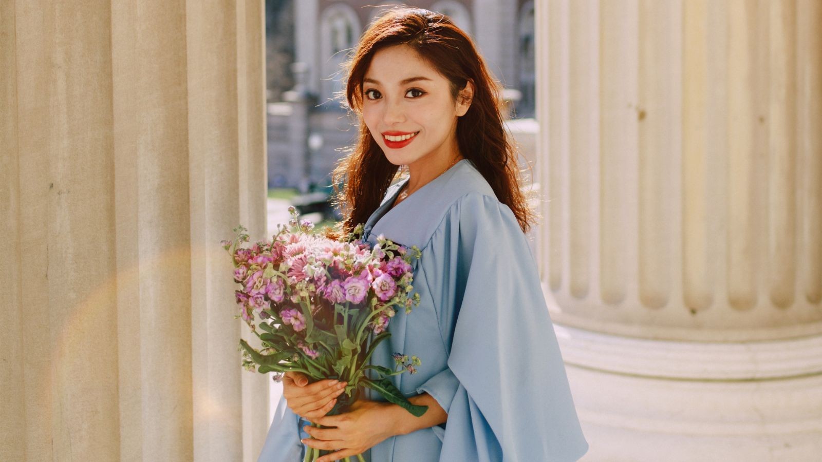 Hanyu holding flowers and posing in cap and gown on the Morningside campus